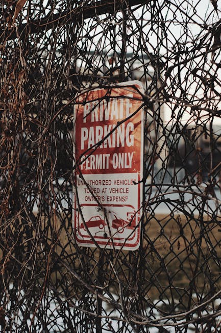 A red and white private parking permit sign mounted on a metal post, partially obscured by a dense tangle of dry, brown, and black thorny branches. The sign indicates that parking is restricted to permit holders only and warns against unauthorized vehicles, including cars and motorcycles, which may be towed at the owner’s expense. The area appears to be an outdoor space adjacent to a property, with a blurred background of an open field and distant buildings under overcast weather. This image illustrates parking restrictions relevant to house removals and relocation services, emphasizing the importance of parking permits and permissions during home moves. Man with Van Old Coulsdon, a company specializing in removals, often manages parking logistics and access issues for residential relocations, ensuring compliance with local parking regulations and facilitating smooth furniture transport and packing and moving processes.