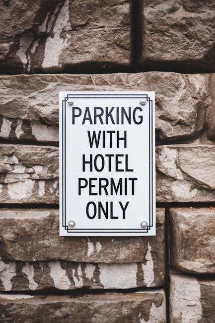 A red and white private parking permit sign mounted on a metal post, partially obscured by a dense tangle of dry, brown, and black thorny branches. The sign indicates that parking is restricted to permit holders only and warns against unauthorized vehicles, including cars and motorcycles, which may be towed at the owner’s expense. The area appears to be an outdoor space adjacent to a property, with a blurred background of an open field and distant buildings under overcast weather. This image illustrates parking restrictions relevant to house removals and relocation services, emphasizing the importance of parking permits and permissions during home moves. Man with Van Old Coulsdon, a company specializing in removals, often manages parking logistics and access issues for residential relocations, ensuring compliance with local parking regulations and facilitating smooth furniture transport and packing and moving processes.